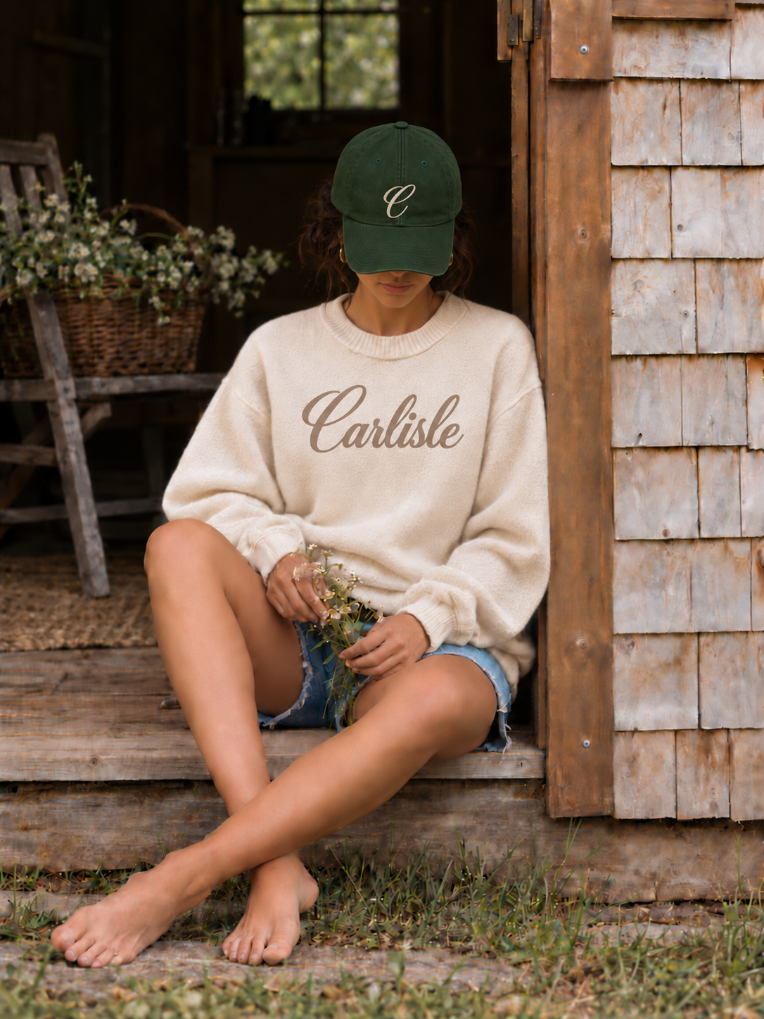 Model in a Forest cap with cursive C embroidery and a cream Carlisle script crew, seated in a doorway